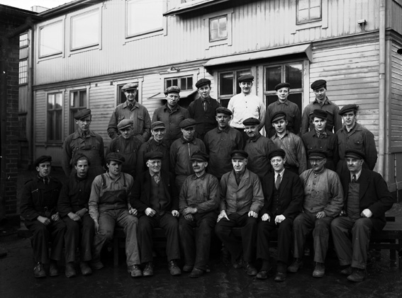 Större samling män iklädda arbetskläder framför fabriksbyggnad.
Fotografens ant: AB. C.J. Wennbergs Mek. Verkstad.
Som ung smedlärling flyttade Carl Johan Wennberg år 1864 till Karlstad. Några år senare startade han en mindre verkstad för reparationer av redskap, vagnar och båtar och därmed lades grunden till företaget, AB C.J Wennbergs Mekaniska Verkstad. På 1890-talet uppfördes ett eget gjuteri i stadsdelen Viken, beläget intill Mariebergsviken.
Källa: Nyblom-Svanqvist, Näringsliv i Värmland, 1945