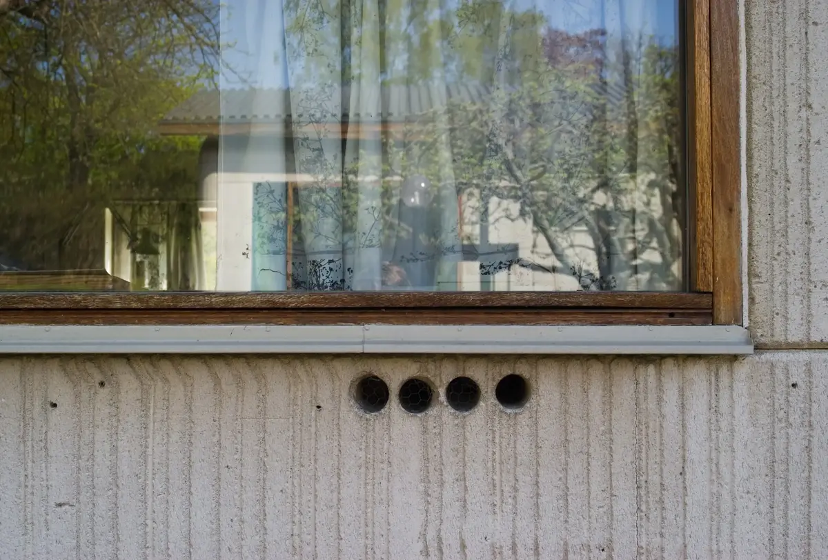 Drottningholm 1:39
Byggnadminne nr: 160
Detalj av vemtilationen på bostadshuset. Hålen är täppta med metallnät och draget regleras innifrån med hjälp av runda träbitar.
Arkitekt  Ralph Erskine; Vernon Gracie. Byggt 1963.