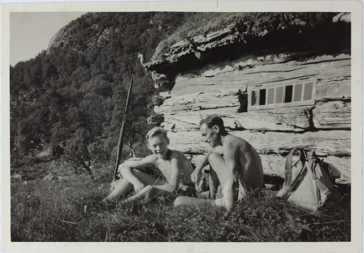 Ein unggut og ein mann sit framføre ein støl (lager for høy) på Fynningsland i Hjelmeland. Frå venstre David Raugstad og Rasmus Rasmussen. Dei tok båt til Lysebotn for å komme dit.