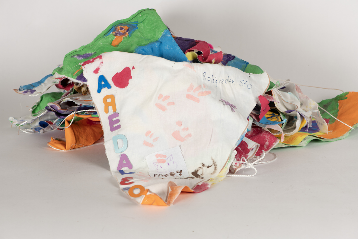 Doble stoff-trekanter dekorert av skoleelever i Arendal, festet til en lang snor. 32 vimpler. Alle har ulik dekor/motiv.