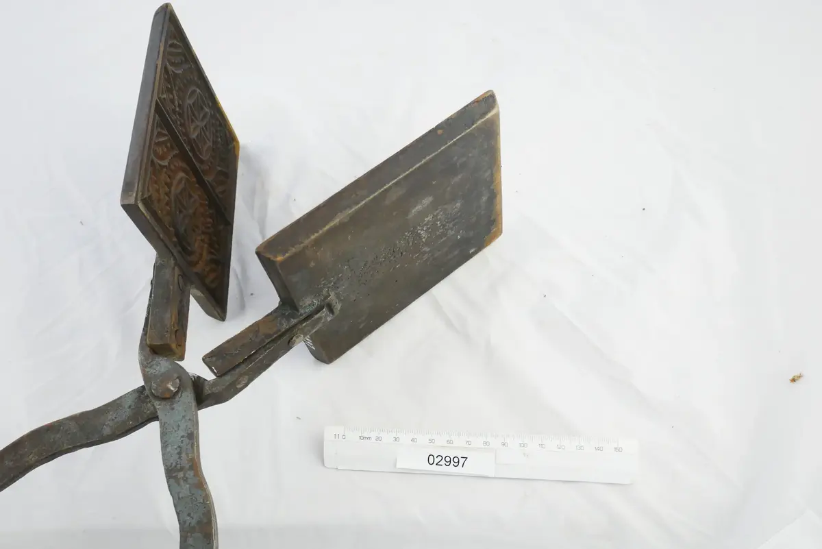 Rånjärn (fyrkantigt) av gjutjärn med långa skänklar,vackert mönstrat inuti järnet med krusiduller.
Troligen avsedd för rånbakning över öppen eld.
Bild 2 visar järnet i öppet läge.