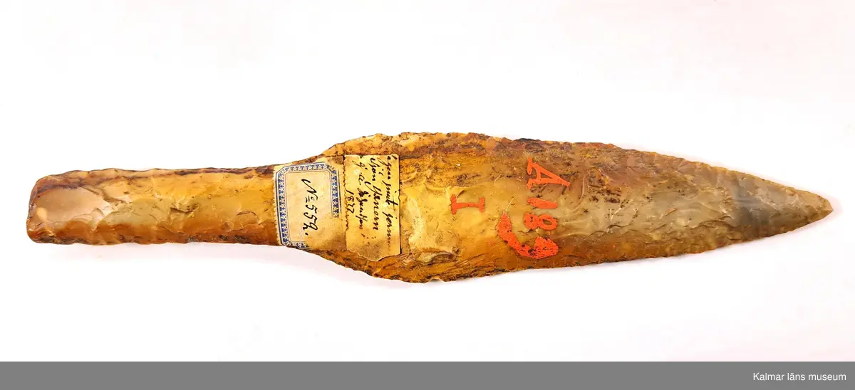 KLM 552. Dolk. Av gulbrun flinta. Senneolitisk tid. Bladet är parallellhugget och insvängt ned mot skaftet. Oskadad. Äldre märkning: A 189 I.