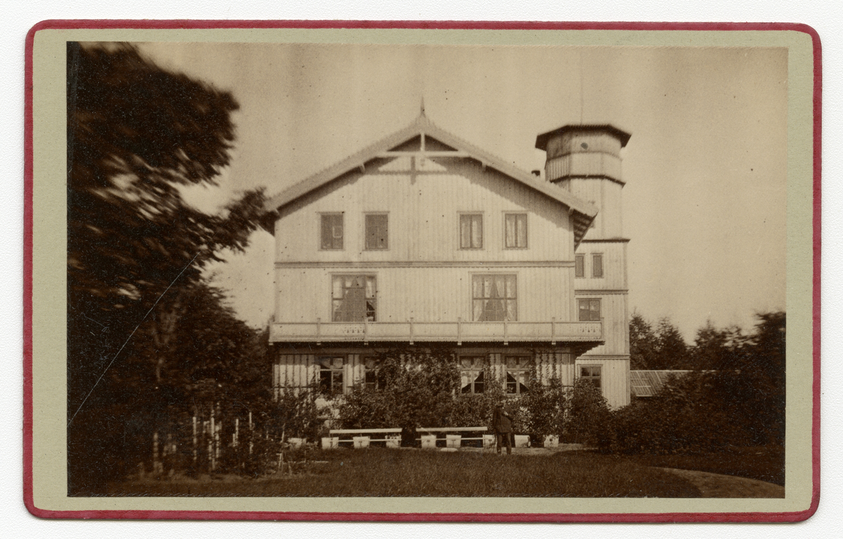 Foto av hus, antagelig på Dal gård i Ullensaker 1880-tallet. En mann står i hagen foran huset