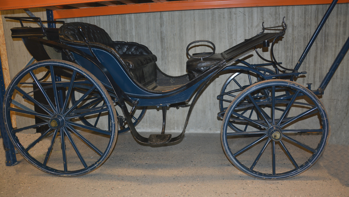Fra protokollen: Trille, for en hest. Plass til 4 personer + kusk bak. Skinntrekk sete. Vogna er utstyrt med brems og har jerngjorder på hjula. Blålakkert med kvite render. Phaeton-trille.