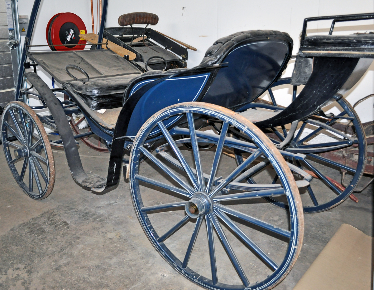 Fra protokollen: Trille, for en hest. Plass til 4 personer + kusk bak. Skinntrekk sete. Vogna er utstyrt med brems og har jerngjorder på hjula. Blålakkert med kvite render. Phaeton-trille.