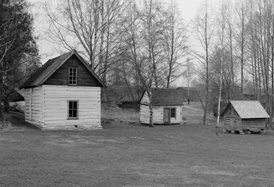Tre en-etasjes tømmerbygningen med noen trær bak. Huset til venstre er hvitkalket i første etasje. Huset i midten er også hvitkalket i gavlen. Bygningen til høyre er glissen mellom tømmer-omfarene.