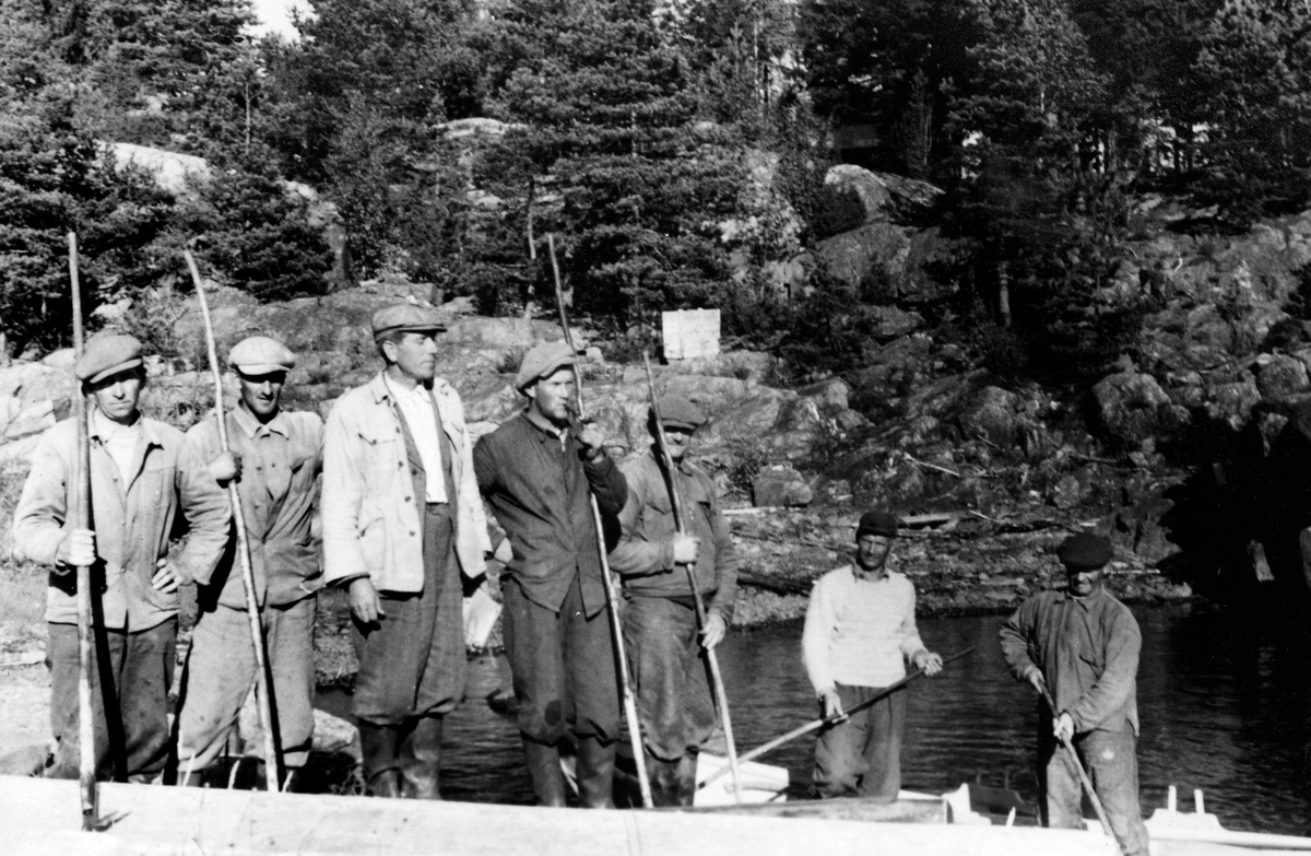 Fløterbasen Johan Enger med det mannskapet som hadde ansvaret for fløtinga på østsida av innsjøen Øyeren i Glommavassdraget sommeren 1952.  De arbeidskledde karene er (fra venstre): Asbjørn Rud, Roald Enger, Johan Enger, Johan Bøhler, Willi Andersen, Jens Svindal og Alfred Bøher.  De to sistnevnte står i en båt, de øvrige står på land, tilsynelatende med en del tømmer foran seg.  I bakgrunnen det berglendte landskapet med spredte trær i revnene som er så typisk for deler av Øyerens nordøstside. 