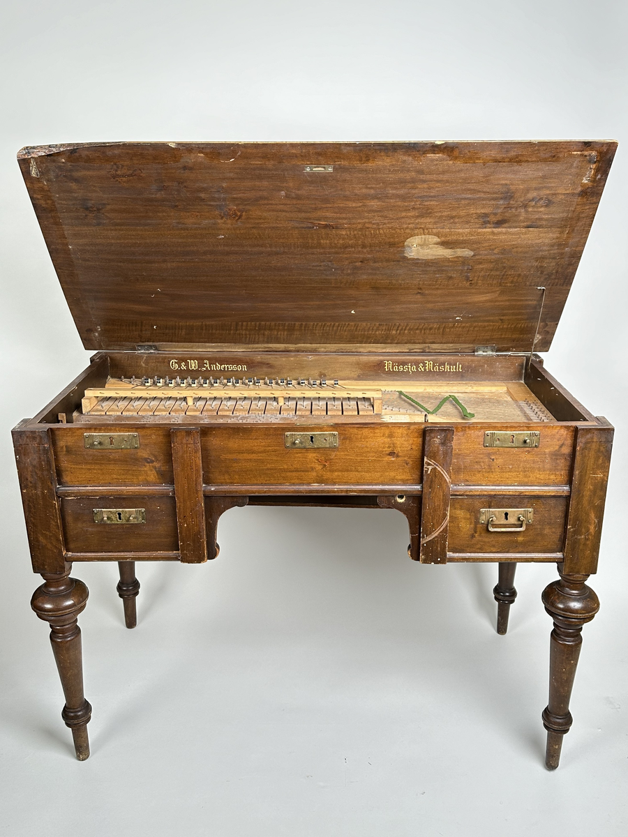 A) Pianoharpa, i form av ett skrivbord av mazarin-typ. Av mörkt betsat och polerat trä. Skrivbordet kraftigt angripet av trägnagare. Svarvade ben och hög sarg, med två utdragbara lådor och tre blindlådor - alla med mässingsbeslag. Bordsskivan uppfällbar och ställbar med metallhake, varunder spelverket med strängar och piggförsedd vals gömmer sig. 
B) och C), två valsar med olika melodier på. Cylinderformade, av trä, med mittaxel och piggar av metall. Valsen snurras med en vev, som lämnat ett svängt märke på möbelns front. 
D), vev av tunn metallarm med ett S-formad avslut i 45 graders vinkel från armen samt svarvad, balusterformat handtag av trä.
E) och F), stämnycklar av metall med fyrkantiga hål, samt enkla handtag av trä. 
G), sprint av metall för att säkra valsen på plats. Tunn, med ögla till avslut.
H), förvaringslåda för melodivals. Av trä, med inbyggd vagga för att hålla valsens mittaxel.