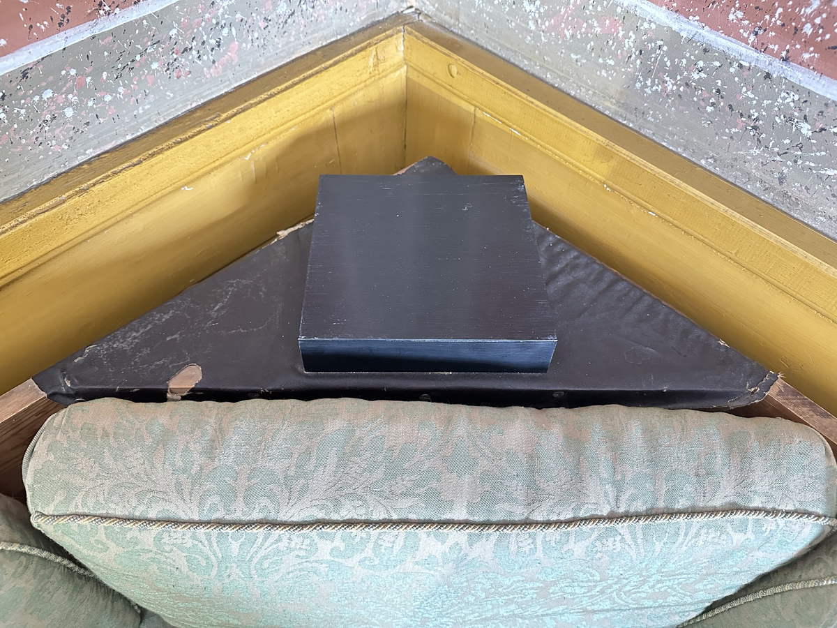 Hörnsoffa i polerad björk med stoppad sits. Genombrutna gavlar med två tvärslåar och spjälor däremellan. Intarsia på gavlarnas kortsidor i form av solfjäderlik halvcirkel samt små rektangulära tegelformade detaljer nederst. Framsargen dekorerad med tunn inläggning i mörkare färg. I hörnets framkant ett svarvat lågt balusterben och något högre sarg med kraftigare inläggning. Ryggen bestående av en sarg baktill med en stödbräda per sida samt en i hörnet. Hörnet klätt i skinnliknande textil och med upphöjd kvadrat i mörkt trä (senare tillkommen). Ribbotten. Sitsar och ryggdynor klädda i lätt glansigt tyg med blomsterornamentik i grön och beige. Kantsnodd i samma kulörer. Baksida i juteväv. 