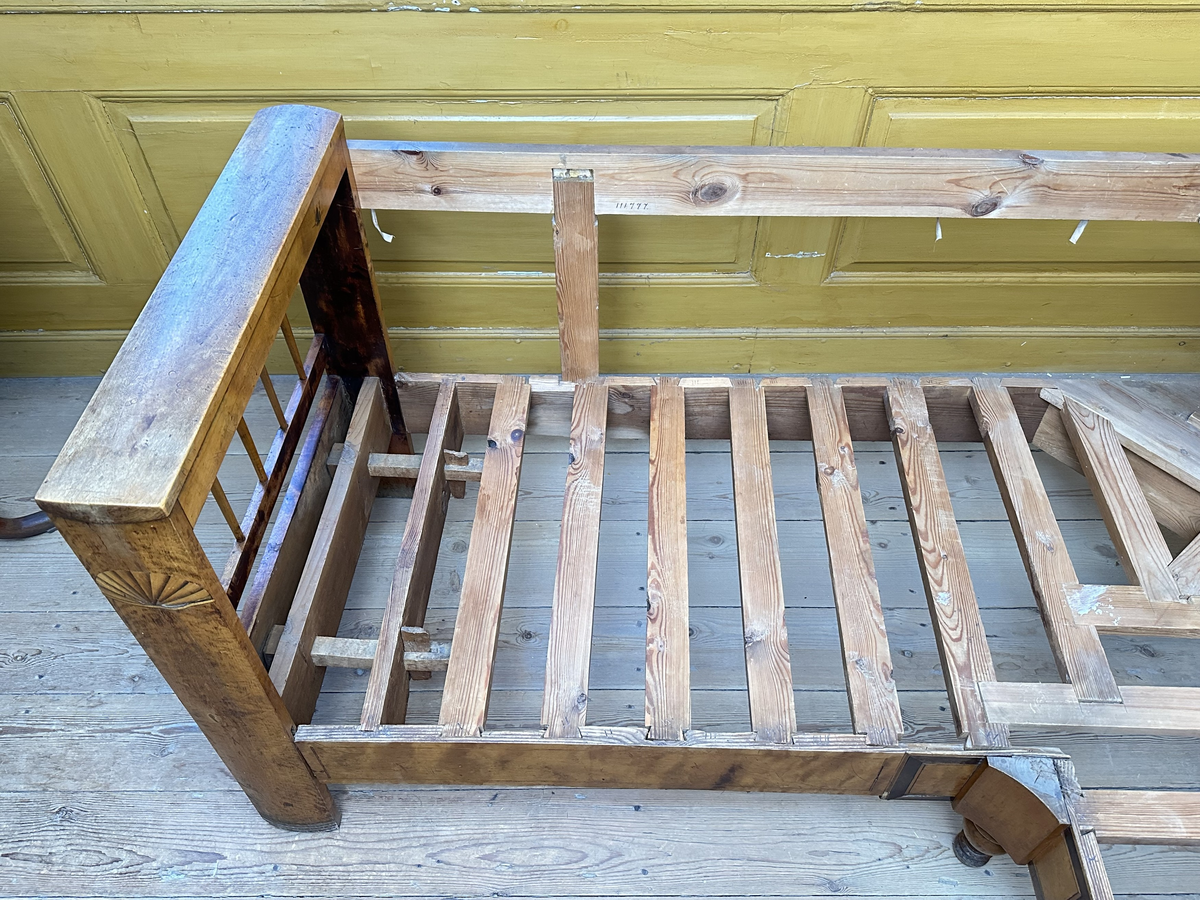 Hörnsoffa i polerad björk med stoppad sits. Genombrutna gavlar med två tvärslåar och spjälor däremellan. Intarsia på gavlarnas kortsidor i form av solfjäderlik halvcirkel samt små rektangulära tegelformade detaljer nederst. Framsargen dekorerad med tunn inläggning i mörkare färg. I hörnets framkant ett svarvat lågt balusterben och något högre sarg med kraftigare inläggning. Ryggen bestående av en sarg baktill med en stödbräda per sida samt en i hörnet. Hörnet klätt i skinnliknande textil och med upphöjd kvadrat i mörkt trä (senare tillkommen). Ribbotten. Sitsar och ryggdynor klädda i lätt glansigt tyg med blomsterornamentik i grön och beige. Kantsnodd i samma kulörer. Baksida i juteväv. 