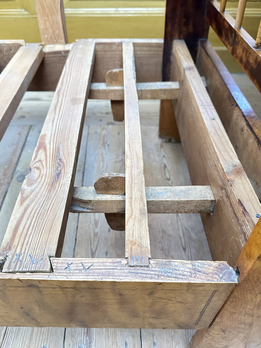 Hörnsoffa i polerad björk med stoppad sits. Genombrutna gavlar med två tvärslåar och spjälor däremellan. Intarsia på gavlarnas kortsidor i form av solfjäderlik halvcirkel samt små rektangulära tegelformade detaljer nederst. Framsargen dekorerad med tunn inläggning i mörkare färg. I hörnets framkant ett svarvat lågt balusterben och något högre sarg med kraftigare inläggning. Ryggen bestående av en sarg baktill med en stödbräda per sida samt en i hörnet. Hörnet klätt i skinnliknande textil och med upphöjd kvadrat i mörkt trä (senare tillkommen). Ribbotten. Sitsar och ryggdynor klädda i lätt glansigt tyg med blomsterornamentik i grön och beige. Kantsnodd i samma kulörer. Baksida i juteväv. 