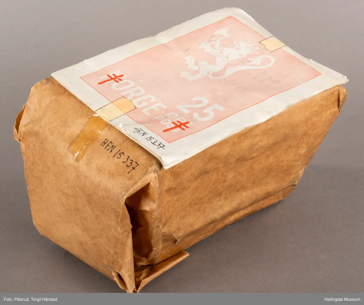 En pakke med uåpne trykksaker til Tubfrim, blant annet årsberetningen for 1949. Pakken er pakket inn med kraftpapir med illustrasjonen til forsiden til årsberetningen utenpå: Et frimerkemotiv med en hvit riksløve på lyserød bakgrunn, under står det Norge og 25 øre post. I tillegg er det plassert to røde Lothringenkors, eller dobbeltkors, i de nederste hjørnene.