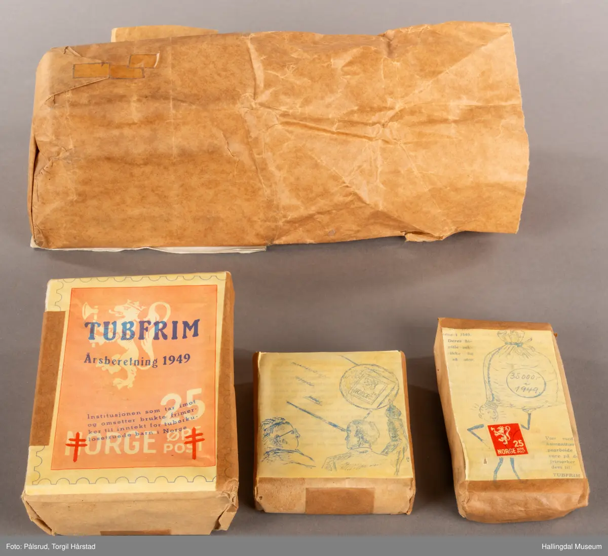 En pakke med uåpne trykksaker til Tubfrim, blant annet årsberetningen for 1949. Pakken er pakket inn med kraftpapir med illustrasjonen til forsiden til årsberetningen utenpå: Et frimerkemotiv med en hvit riksløve på lyserød bakgrunn, under står det Norge og 25 øre post. I tillegg er det plassert to røde Lothringenkors, eller dobbeltkors, i de nederste hjørnene.