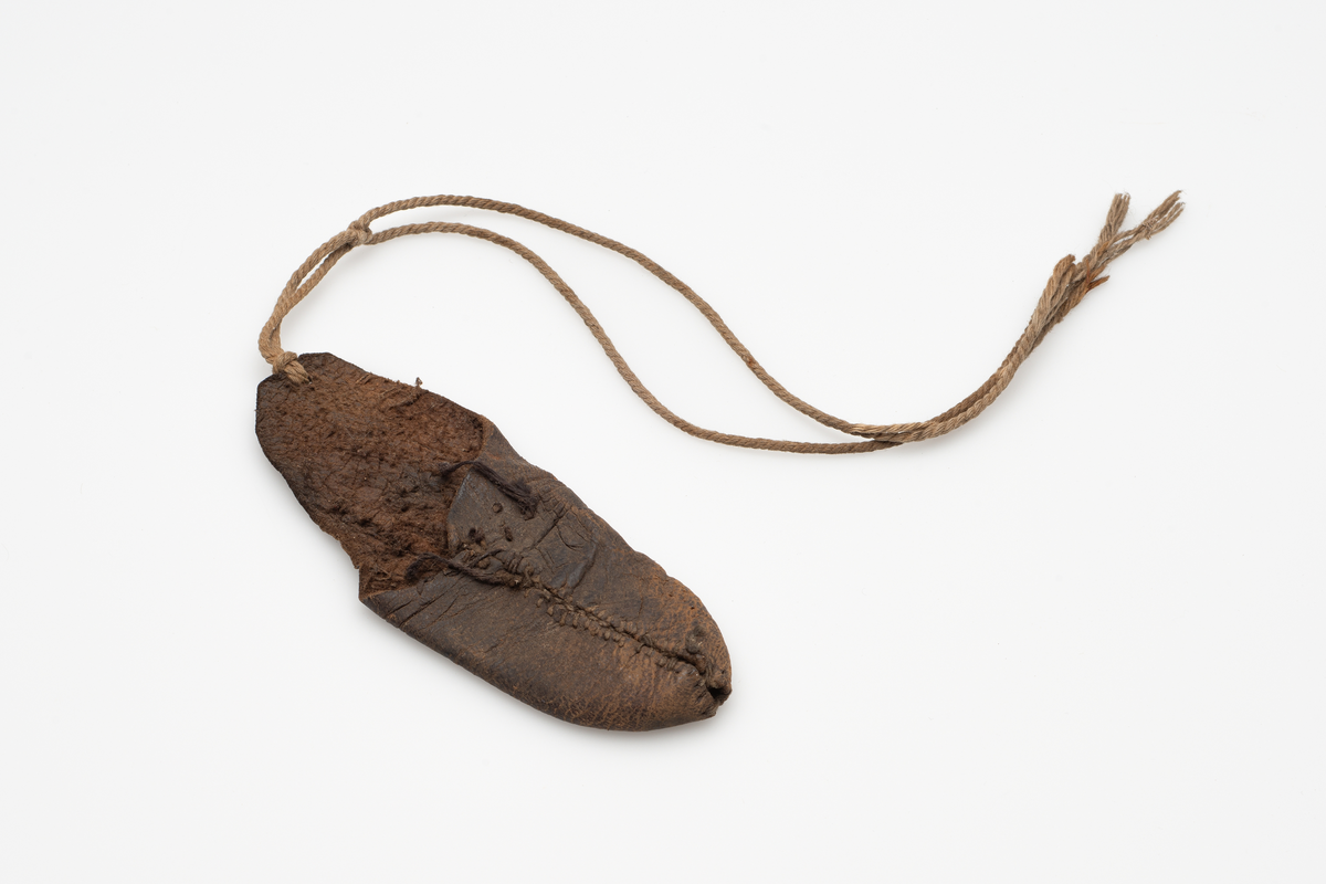 Fingerbeskyttelse av skinn. Skinnet sydd sammen til en fingerformet hylse, den ene kanten lengre enn den andre. Tråd festet til den lengre kanten, antagelig for å knyte runt håndleddet.