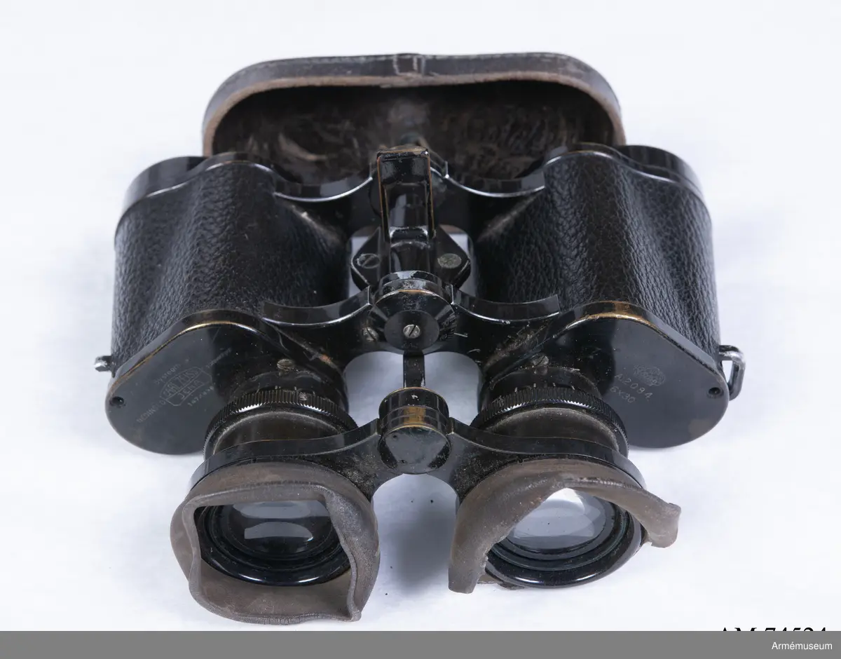 Dubbelkikare för militärt bruk av märket Carl Zeiss Jena Nedinsco samt tillhörande fodral. Kikarfodralet är av märket Busch och samhör inte ursprungligen med själva kikaren. 

´s-Gravenhage är det äldre officiella namnet på Haag, vilket står inpräntat på föremålet.

Märkningen ”A” står högst troligt för Artilleriet. Kronmärkt vilket stämplades redan vid tillverkningen i fabriken i Nederländerna. Övriga kikarmodeller i serien beställdes av svenska flottan i 7x50 förstoring och för danska försvaret i 8x40.
6x30: Siffran 6 avser själva förstoringen alternativt att det iakttagna föremålet i kikaren upplevs vara 6 gånger närmare än i verkligheten. 30 avser diametern i millimeter på frontlinsen längst fram på kikaren där ljusinsläppet sker. 

Exemplaret har extra stora ögonlinser vilket underlättar hanteringen då kikaren ska användas i kombination med gasmask. Kikaren kan då inte läggas an direkt mot ögonen utan måste hållas mot gasmasken. Föremålet är det enda kända kvarvarande i den här förstoringen i kombination med den särskilda bygeln på ovansidan avsedd att manövrera gasmaskokularet fram och tillbaka. Konstruktionen med bygeln fungerade inte särskilt väl eftersom den både var skör och svårmanövrerad, varpå bygeln senare togs bort. Exemplaret skiljer sig gentemot andra liknande kikarmodeller som har vita gasmaskokular. 

Vid observation i kikaren kan den särskilda streckskalan skönjas i det vänstra okularet med numrering 0-100 horisontellt och 0-20 vertikalt. Hjälpmedlet underlättar avståndsbedömningar av verkliga föremål i terrängen eller över vattenytan. 

Grupp F III.
Kikare märkt "Systeem Nedinsco Carl Zeiss Jena S. Gravenhage 1474936" och "Krona A:2084 6x30".