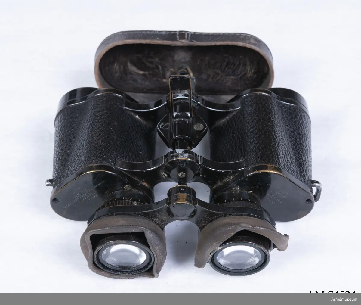 Dubbelkikare för militärt bruk av märket Carl Zeiss Jena Nedinsco samt tillhörande fodral. Kikarfodralet är av märket Busch och samhör inte ursprungligen med själva kikaren. 

´s-Gravenhage är det äldre officiella namnet på Haag, vilket står inpräntat på föremålet.

Märkningen ”A” står högst troligt för Artilleriet. Kronmärkt vilket stämplades redan vid tillverkningen i fabriken i Nederländerna. Övriga kikarmodeller i serien beställdes av svenska flottan i 7x50 förstoring och för danska försvaret i 8x40.
6x30: Siffran 6 avser själva förstoringen alternativt att det iakttagna föremålet i kikaren upplevs vara 6 gånger närmare än i verkligheten. 30 avser diametern i millimeter på frontlinsen längst fram på kikaren där ljusinsläppet sker. 

Exemplaret har extra stora ögonlinser vilket underlättar hanteringen då kikaren ska användas i kombination med gasmask. Kikaren kan då inte läggas an direkt mot ögonen utan måste hållas mot gasmasken. Föremålet är det enda kända kvarvarande i den här förstoringen i kombination med den särskilda bygeln på ovansidan avsedd att manövrera gasmaskokularet fram och tillbaka. Konstruktionen med bygeln fungerade inte särskilt väl eftersom den både var skör och svårmanövrerad, varpå bygeln senare togs bort. Exemplaret skiljer sig gentemot andra liknande kikarmodeller som har vita gasmaskokular. 

Vid observation i kikaren kan den särskilda streckskalan skönjas i det vänstra okularet med numrering 0-100 horisontellt och 0-20 vertikalt. Hjälpmedlet underlättar avståndsbedömningar av verkliga föremål i terrängen eller över vattenytan. 

Grupp F III.
Kikare märkt "Systeem Nedinsco Carl Zeiss Jena S. Gravenhage 1474936" och "Krona A:2084 6x30".