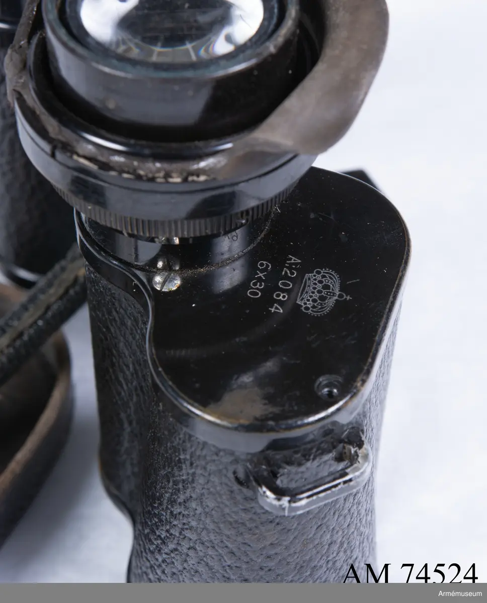 Dubbelkikare för militärt bruk av märket Carl Zeiss Jena Nedinsco samt tillhörande fodral. Kikarfodralet är av märket Busch och samhör inte ursprungligen med själva kikaren. 

´s-Gravenhage är det äldre officiella namnet på Haag, vilket står inpräntat på föremålet.

Märkningen ”A” står högst troligt för Artilleriet. Kronmärkt vilket stämplades redan vid tillverkningen i fabriken i Nederländerna. Övriga kikarmodeller i serien beställdes av svenska flottan i 7x50 förstoring och för danska försvaret i 8x40.
6x30: Siffran 6 avser själva förstoringen alternativt att det iakttagna föremålet i kikaren upplevs vara 6 gånger närmare än i verkligheten. 30 avser diametern i millimeter på frontlinsen längst fram på kikaren där ljusinsläppet sker. 

Exemplaret har extra stora ögonlinser vilket underlättar hanteringen då kikaren ska användas i kombination med gasmask. Kikaren kan då inte läggas an direkt mot ögonen utan måste hållas mot gasmasken. Föremålet är det enda kända kvarvarande i den här förstoringen i kombination med den särskilda bygeln på ovansidan avsedd att manövrera gasmaskokularet fram och tillbaka. Konstruktionen med bygeln fungerade inte särskilt väl eftersom den både var skör och svårmanövrerad, varpå bygeln senare togs bort. Exemplaret skiljer sig gentemot andra liknande kikarmodeller som har vita gasmaskokular. 

Vid observation i kikaren kan den särskilda streckskalan skönjas i det vänstra okularet med numrering 0-100 horisontellt och 0-20 vertikalt. Hjälpmedlet underlättar avståndsbedömningar av verkliga föremål i terrängen eller över vattenytan. 

Grupp F III.
Kikare märkt "Systeem Nedinsco Carl Zeiss Jena S. Gravenhage 1474936" och "Krona A:2084 6x30".
