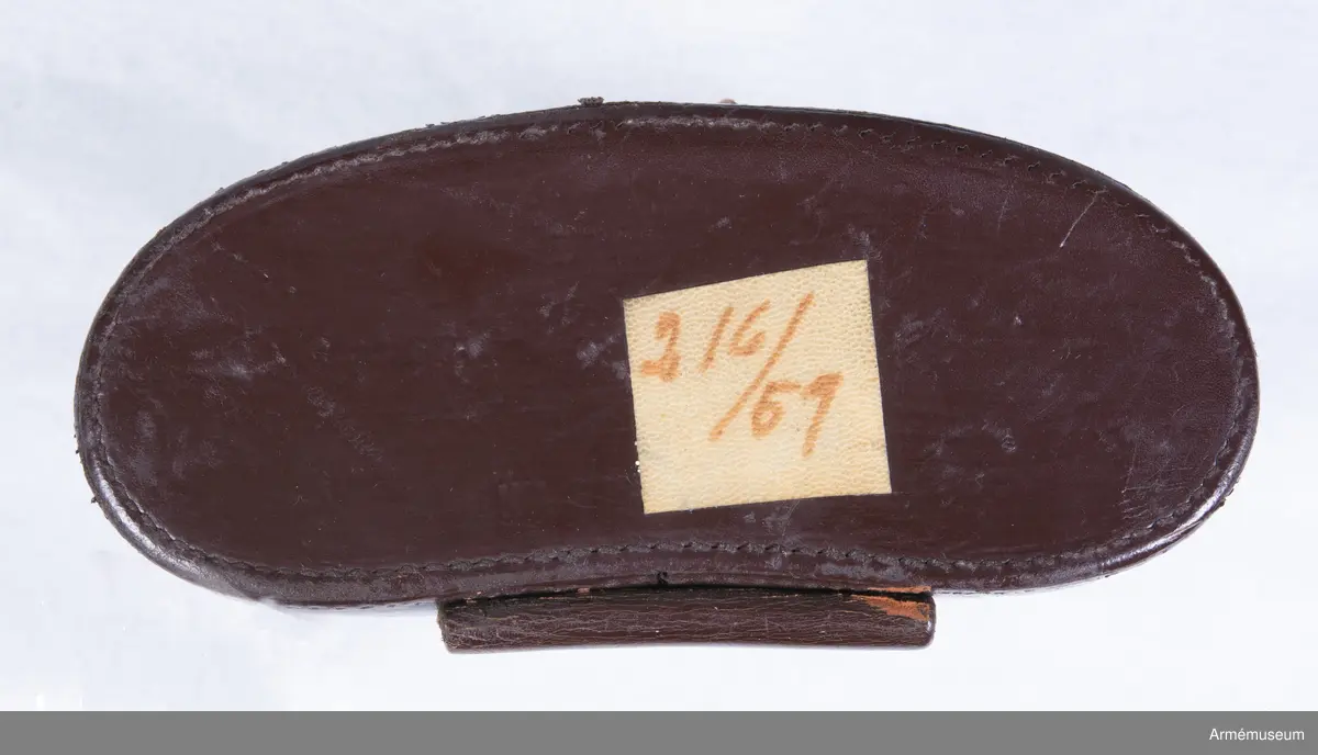 Dubbelkikare för militärt bruk av märket Carl Zeiss Jena Nedinsco samt tillhörande fodral. Kikarfodralet är av märket Busch och samhör inte ursprungligen med själva kikaren. 

´s-Gravenhage är det äldre officiella namnet på Haag, vilket står inpräntat på föremålet.

Märkningen ”A” står högst troligt för Artilleriet. Kronmärkt vilket stämplades redan vid tillverkningen i fabriken i Nederländerna. Övriga kikarmodeller i serien beställdes av svenska flottan i 7x50 förstoring och för danska försvaret i 8x40.
6x30: Siffran 6 avser själva förstoringen alternativt att det iakttagna föremålet i kikaren upplevs vara 6 gånger närmare än i verkligheten. 30 avser diametern i millimeter på frontlinsen längst fram på kikaren där ljusinsläppet sker. 

Exemplaret har extra stora ögonlinser vilket underlättar hanteringen då kikaren ska användas i kombination med gasmask. Kikaren kan då inte läggas an direkt mot ögonen utan måste hållas mot gasmasken. Föremålet är det enda kända kvarvarande i den här förstoringen i kombination med den särskilda bygeln på ovansidan avsedd att manövrera gasmaskokularet fram och tillbaka. Konstruktionen med bygeln fungerade inte särskilt väl eftersom den både var skör och svårmanövrerad, varpå bygeln senare togs bort. Exemplaret skiljer sig gentemot andra liknande kikarmodeller som har vita gasmaskokular. 

Vid observation i kikaren kan den särskilda streckskalan skönjas i det vänstra okularet med numrering 0-100 horisontellt och 0-20 vertikalt. Hjälpmedlet underlättar avståndsbedömningar av verkliga föremål i terrängen eller över vattenytan. 

Grupp F III.
Kikare märkt "Systeem Nedinsco Carl Zeiss Jena S. Gravenhage 1474936" och "Krona A:2084 6x30".
