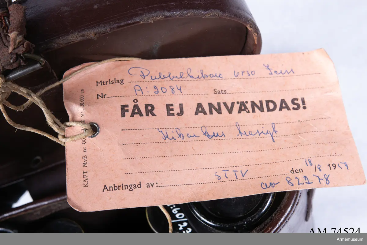 Dubbelkikare för militärt bruk av märket Carl Zeiss Jena Nedinsco samt tillhörande fodral. Kikarfodralet är av märket Busch och samhör inte ursprungligen med själva kikaren. 

´s-Gravenhage är det äldre officiella namnet på Haag, vilket står inpräntat på föremålet.

Märkningen ”A” står högst troligt för Artilleriet. Kronmärkt vilket stämplades redan vid tillverkningen i fabriken i Nederländerna. Övriga kikarmodeller i serien beställdes av svenska flottan i 7x50 förstoring och för danska försvaret i 8x40.
6x30: Siffran 6 avser själva förstoringen alternativt att det iakttagna föremålet i kikaren upplevs vara 6 gånger närmare än i verkligheten. 30 avser diametern i millimeter på frontlinsen längst fram på kikaren där ljusinsläppet sker. 

Exemplaret har extra stora ögonlinser vilket underlättar hanteringen då kikaren ska användas i kombination med gasmask. Kikaren kan då inte läggas an direkt mot ögonen utan måste hållas mot gasmasken. Föremålet är det enda kända kvarvarande i den här förstoringen i kombination med den särskilda bygeln på ovansidan avsedd att manövrera gasmaskokularet fram och tillbaka. Konstruktionen med bygeln fungerade inte särskilt väl eftersom den både var skör och svårmanövrerad, varpå bygeln senare togs bort. Exemplaret skiljer sig gentemot andra liknande kikarmodeller som har vita gasmaskokular. 

Vid observation i kikaren kan den särskilda streckskalan skönjas i det vänstra okularet med numrering 0-100 horisontellt och 0-20 vertikalt. Hjälpmedlet underlättar avståndsbedömningar av verkliga föremål i terrängen eller över vattenytan. 

Grupp F III.
Kikare märkt "Systeem Nedinsco Carl Zeiss Jena S. Gravenhage 1474936" och "Krona A:2084 6x30".