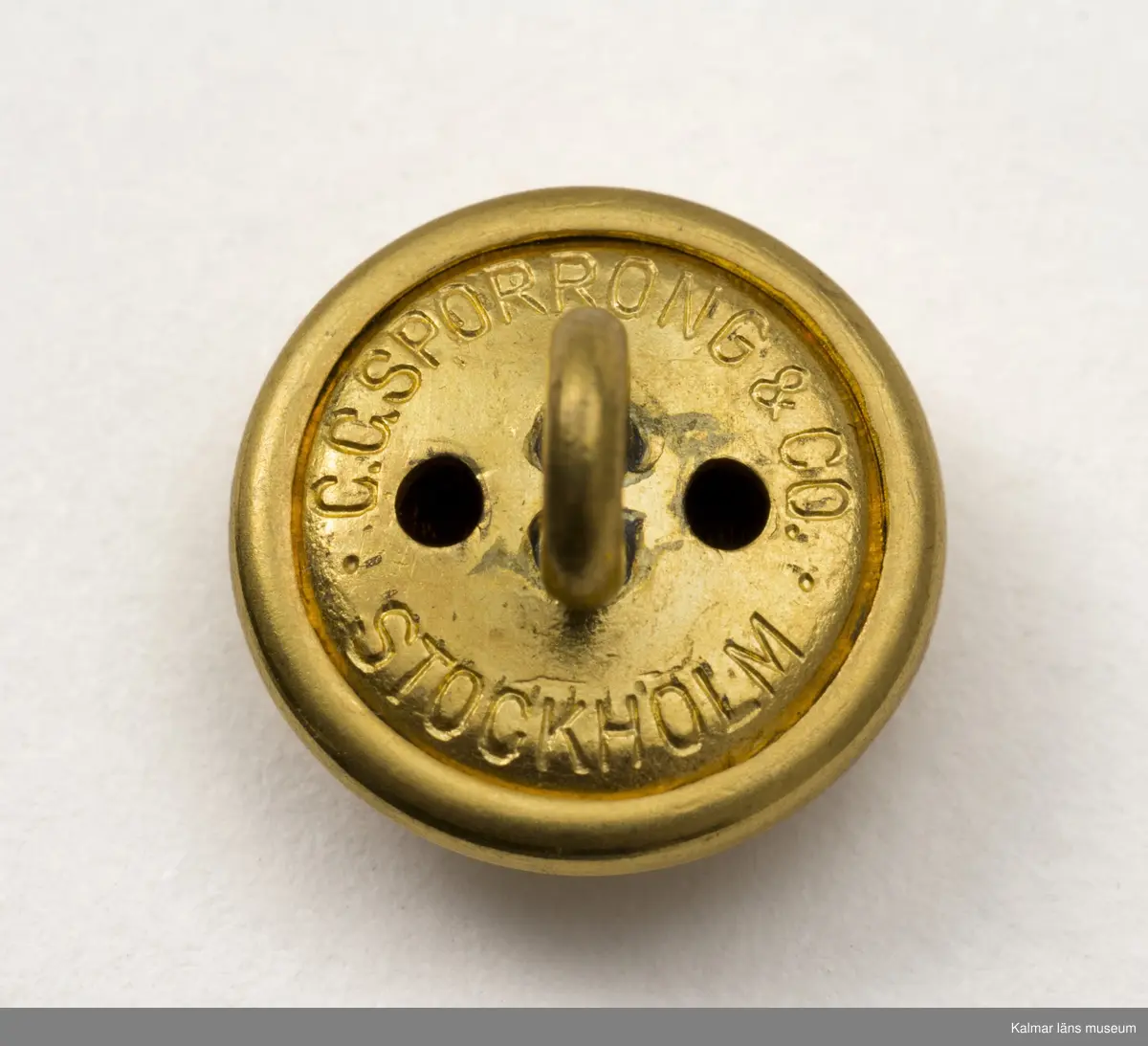KLM 44534:24:1-2. Knapp, uniformstillbehör, 10 st. Åtta knappar och två manschettknappar. I ena fickan på Väst KLM 44534:4 hittades en ziplock-påse med åtta lösa små guldfärgade kulknappar med tre kronor och ett par manschettknappar med flygvapnets vapen på blå emalj, märkta med ÅT (Åke Torudd). Använda tillsammans med väst KLM 44534:4.