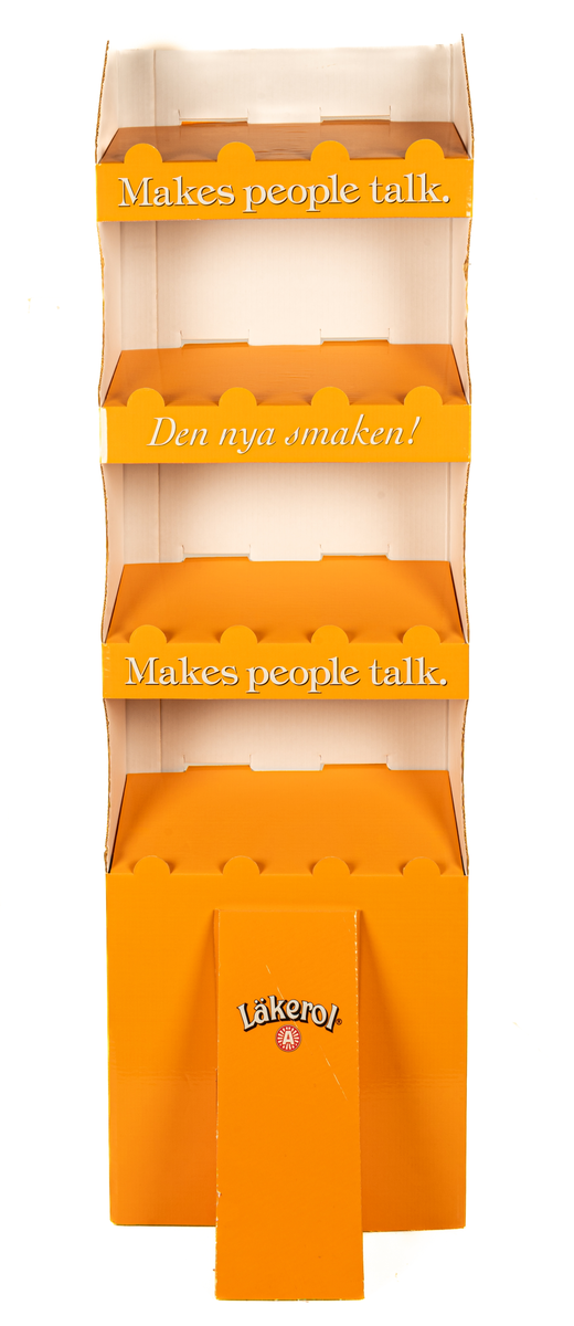 Reklamställ i papp, orange och vitt. Fyra fack för reklamartiklar. Tryckt text: Läkerol Make people talk.
