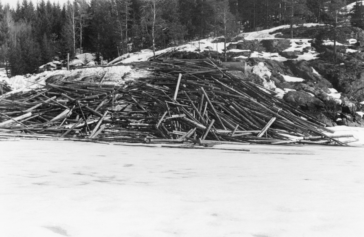 Tømmervelte ved Sæter i Trøgstad kommune i Østfold vinteren 1954.  Fotografiet viser hvordan tømmeret er veltet fra en bergrygg mot den islagte og snødekte flata på innsjøen Øyeren.  Stokkene ligger hulter til bulter, dels i skråningen ned mot vassdraget, dels på isen.  En slik måte å velte fra seg fløtingstømmer på innebar mye besvær for fløterne.  De stokkene som ble liggende på sjøen ville lett drive av gårde når isen gikk, før man rakk å "soppe" (bunte) dem, de som lå hulter til bulter i skråningen ned mot stranda ble det tungt og vanskelig å få på vannet.  Tømmerveltene skulle helst ligge luftig til på strandbrinken, med stokkenes lengderetning parallelt, slik at de lettvint kunne rulles uti når tida var moden for det.  Dette fotografiet ble antakelig tatt for å få leverandøren (i dette tilfellet Borregaard) til å innskjerpe slike rutiner for sine folk. 