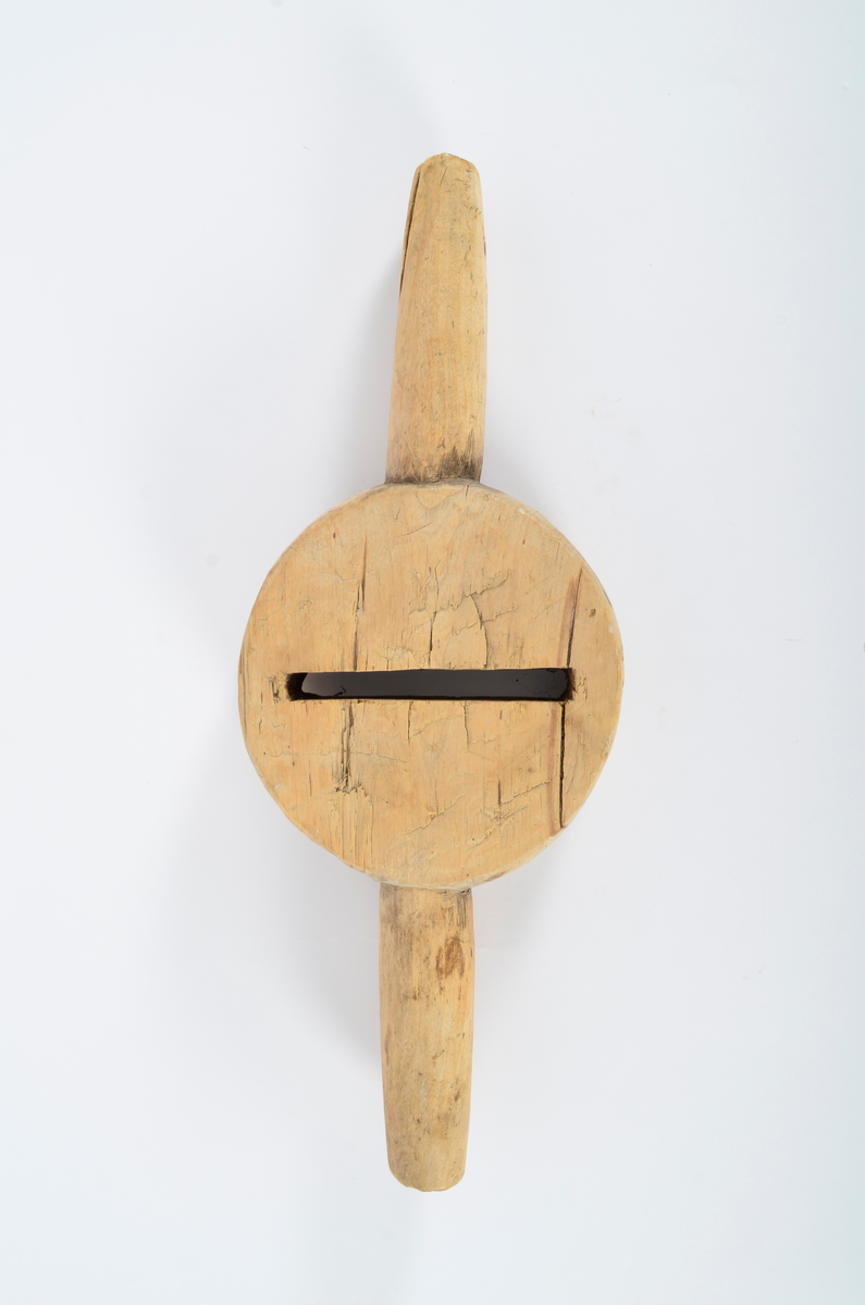 Består av sirkulær kloss med gjennombrutt smal fure i sentrum, ca. 12 cm lang. Horisontalt på furen, to runde håndtak. Smalner utover. Umalt.
