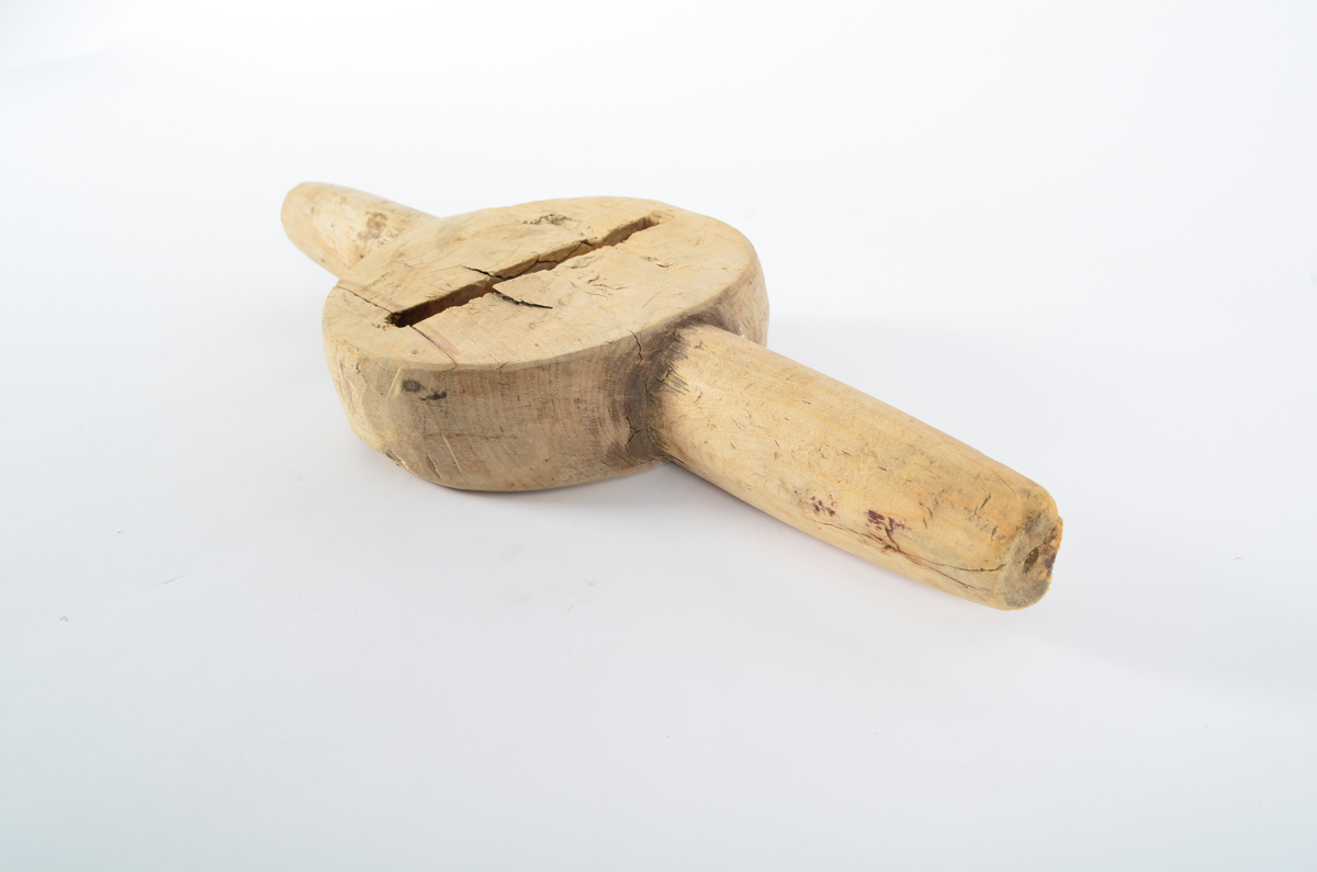 Består av sirkulær kloss med gjennombrutt smal fure i sentrum, ca. 12 cm lang. Horisontalt på furen, to runde håndtak. Smalner utover. Umalt.