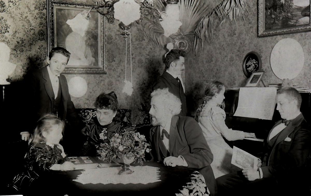 Ved bordet: Myntgravør Ivar Trondsen (1853-1932) og kona Inga Marie Josefine Hansen (1856-1926) m/fam. Datteren, Hjørdis f.1889, ser på bilder.
Trondsen's to døtre var gift med bergmester Ragnvald Støren og med høyesterettsadvokat Kr. Nauf.
