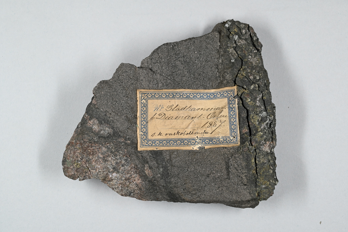 Malmprov, grå. Märkt med påklistrad lapp: "No. Gladhammar, f (?) Diamant-orten, 1887. s. k. ruskoboltmalm".