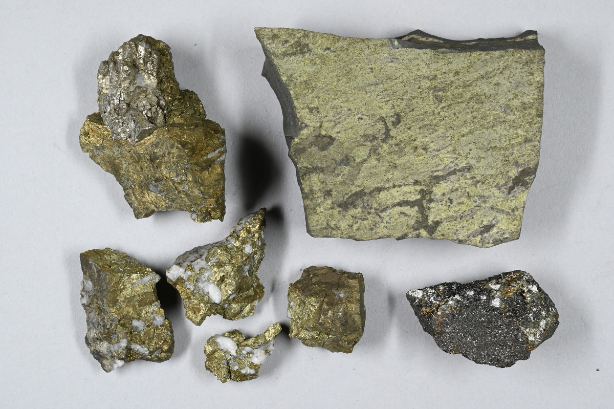 Sju materialprover. En grå och grönaktig, fem grön och vitaktiga och en gråaktig med skimmer. Tillhörande lapp med notering: "Ugnsgalmeja, Åtvidaberg, 1873".