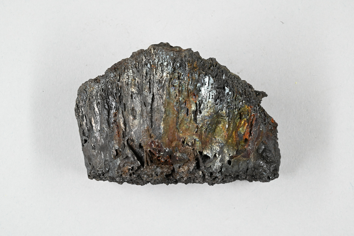 Prov av järnslagg, svart med metallisk glans. Tillhörande lapp med notering: "21. Eisenfrischschlacke".
