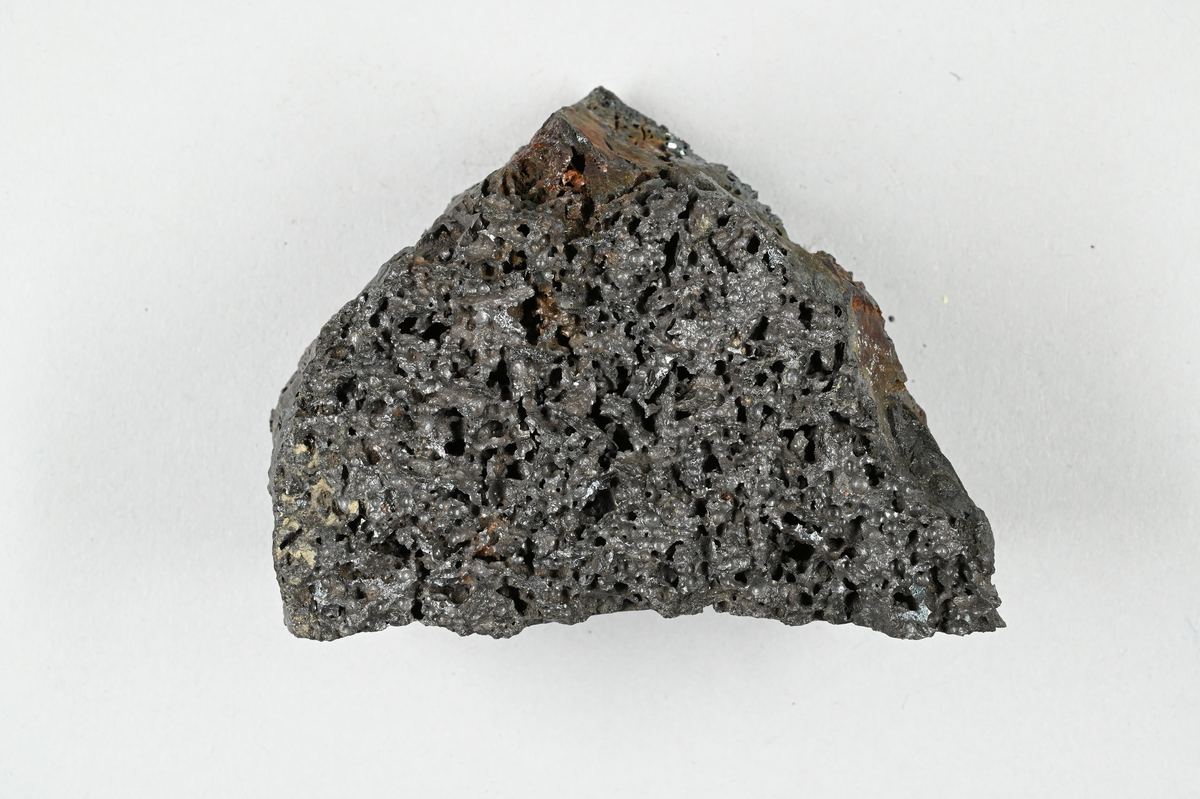 Prov av järnslagg, svart med metallisk glans. Tillhörande lapp med notering: "21. Eisenfrischschlacke".