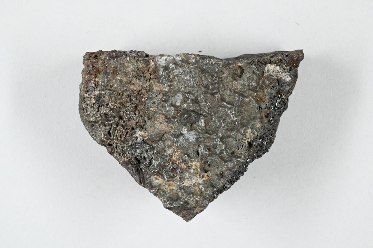 Prov av järnslagg, svart med metallisk glans. Tillhörande lapp med notering: "21. Eisenfrischschlacke".