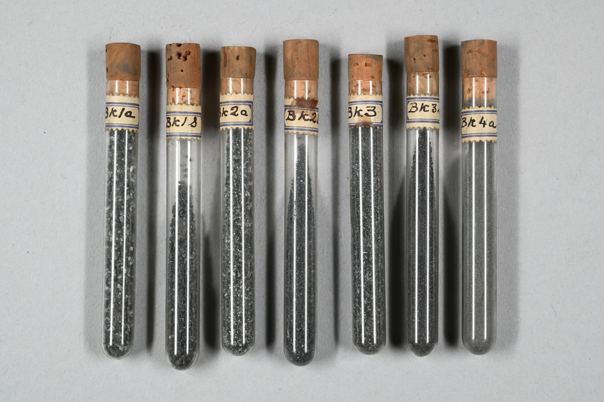 Flera provrör med mineral i olika pulverformer, grå. Vissa prover magnetiska. Provrör märkta med påklistrad lapp: "Ak1", "Ak1S", Ak2S", "Ak3", Ak3a", Ak3S", "Ak4", "Ak4a", "Ak4S", "Bk1a", "Bk1S", "Bk2a", "Bk2S", "Bk3", "Bk3S", "Bk4a", "Ck1", "Ck1a", "Ck1S", "Ck2a", "Ck3", "Ck3S", "Ck4", "Ck4S", "Dk1a", "Dk1S", Dk2S", "Dk4S", "B", "D", "Slam" och "B Slam".