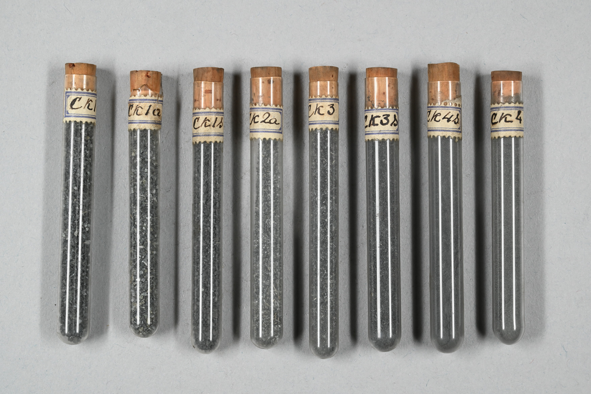 Flera provrör med mineral i olika pulverformer, grå. Vissa prover magnetiska. Provrör märkta med påklistrad lapp: "Ak1", "Ak1S", Ak2S", "Ak3", Ak3a", Ak3S", "Ak4", "Ak4a", "Ak4S", "Bk1a", "Bk1S", "Bk2a", "Bk2S", "Bk3", "Bk3S", "Bk4a", "Ck1", "Ck1a", "Ck1S", "Ck2a", "Ck3", "Ck3S", "Ck4", "Ck4S", "Dk1a", "Dk1S", Dk2S", "Dk4S", "B", "D", "Slam" och "B Slam".