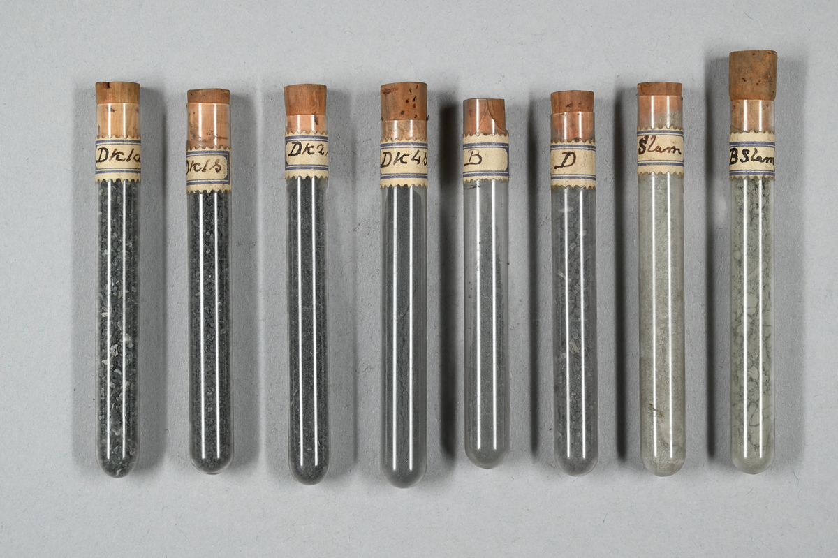Flera provrör med mineral i olika pulverformer, grå. Vissa prover magnetiska. Provrör märkta med påklistrad lapp: "Ak1", "Ak1S", Ak2S", "Ak3", Ak3a", Ak3S", "Ak4", "Ak4a", "Ak4S", "Bk1a", "Bk1S", "Bk2a", "Bk2S", "Bk3", "Bk3S", "Bk4a", "Ck1", "Ck1a", "Ck1S", "Ck2a", "Ck3", "Ck3S", "Ck4", "Ck4S", "Dk1a", "Dk1S", Dk2S", "Dk4S", "B", "D", "Slam" och "B Slam".