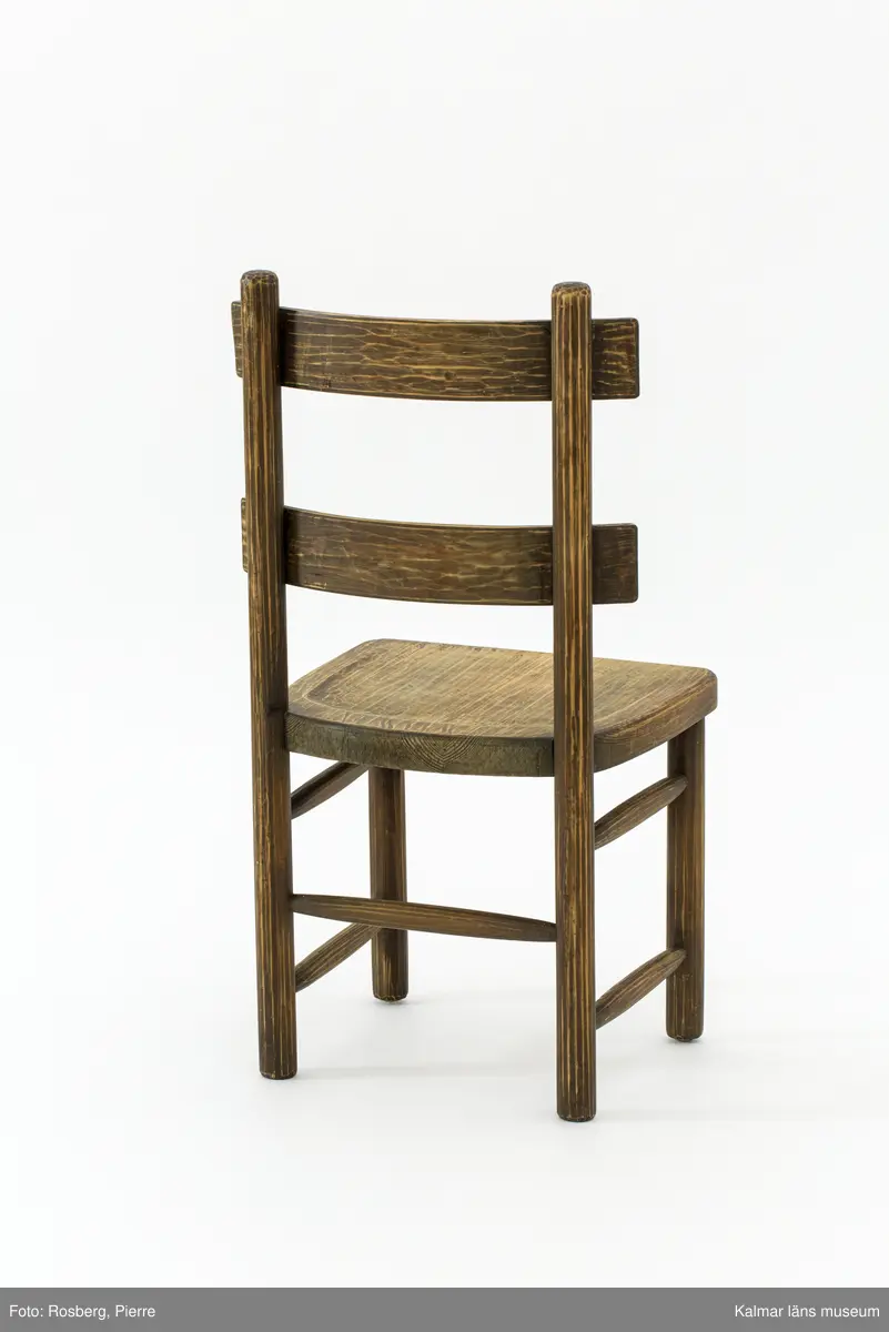 KLM 46378:3. Stol. Ingår i möbelserien "Sandhamn". Av furu med brunbetsad yta som senare även slipats. Skålad sits. Ryggen består av två ribbor fastsatta med smidda järnspikar, ena spikhuvudet saknas. Under stolssitsen en rektangulär metallbricka med text: AB NORDISKA KOMPANIET R 33845- MÖB.