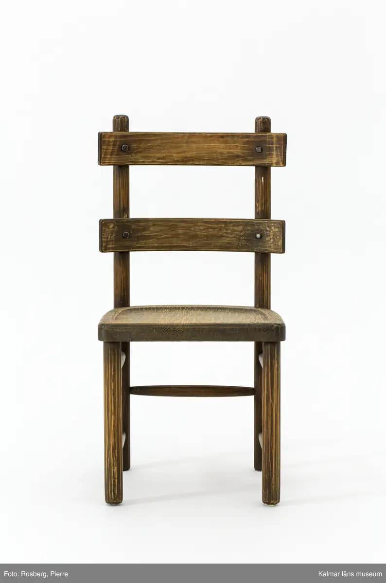 KLM 46378:3. Stol. Ingår i möbelserien "Sandhamn". Av furu med brunbetsad yta som senare även slipats. Skålad sits. Ryggen består av två ribbor fastsatta med smidda järnspikar, ena spikhuvudet saknas. Under stolssitsen en rektangulär metallbricka med text: AB NORDISKA KOMPANIET R 33845- MÖB.