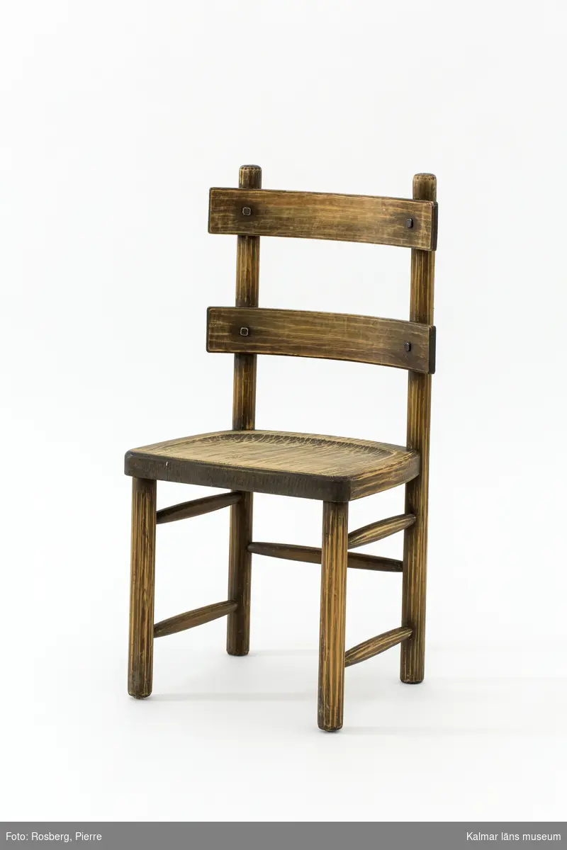 KLM 46378:4. Stol. Ingår i möbelserien "Sandhamn". Av furu med brunbetsad yta som senare även slipats. Skålad sits. Ryggen består av två ribbor fastsatta med smidda järnspikar. Under stolssitsen en rektangulär metallbricka med text: AB NORDISKA KOMPANIET R 33845- MÖB.