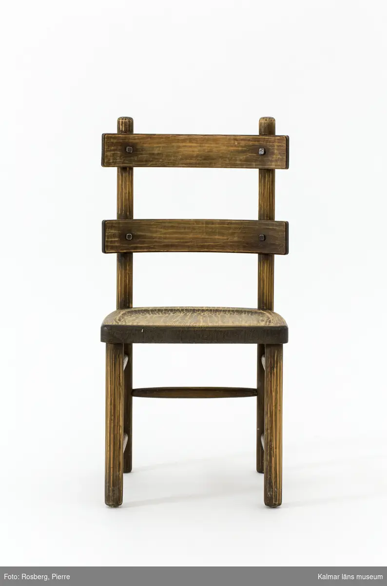 KLM 46378:4. Stol. Ingår i möbelserien "Sandhamn". Av furu med brunbetsad yta som senare även slipats. Skålad sits. Ryggen består av två ribbor fastsatta med smidda järnspikar. Under stolssitsen en rektangulär metallbricka med text: AB NORDISKA KOMPANIET R 33845- MÖB.