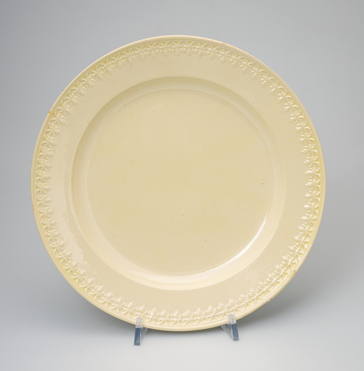 En flat tallerken av glasert steintøy (creamware). Den er hvitgul på farge (ensfarget). Flaten på midten er 16,5cm i diameter. Langs kanten er det tungekant. Innenfor tungekanten er det støpt dekor i form av en hjertebord med stiliserte blomster/bladverk. På undersiden er det dypstempel i form av fire små hjerteformede prikker i klase (utgjør en sirkerl) som er et pottemakermerke.