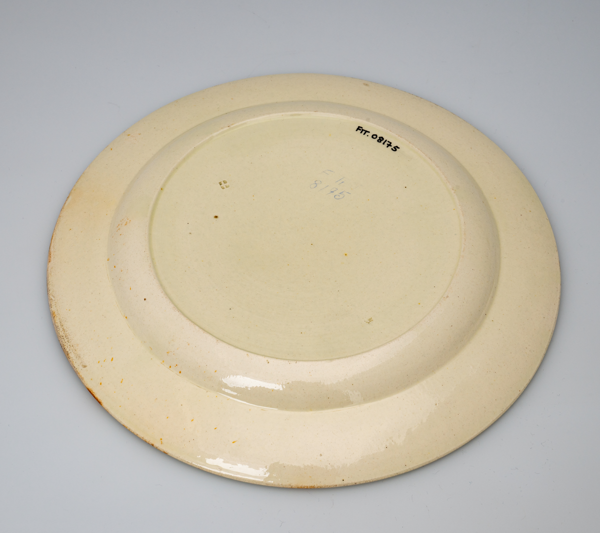 En flat tallerken av glasert steintøy (creamware). Den er hvitgul på farge (ensfarget). Flaten på midten er 16,5cm i diameter. Langs kanten er det tungekant. Innenfor tungekanten er det støpt dekor i form av en hjertebord med stiliserte blomster/bladverk. På undersiden er det dypstempel i form av fire små ruter/prikker i klase som er et pottemakermerke.