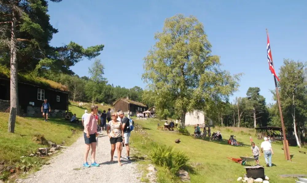 Mange mennesker sommerkledt i fint sommervær på Olsokstevne på Gamle Kvernes bygdemuseum