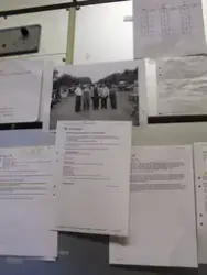 Några dokument och ett fotografi är uppsatta på en vägg. Int