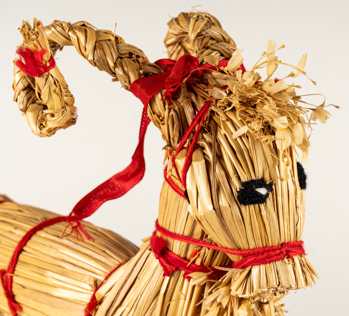 Julbock av halm, halmbock. Flätade horn och svans. Bocken är hopbunden med röda bomullsband. Ögon påsydda med svart och vitt garn.