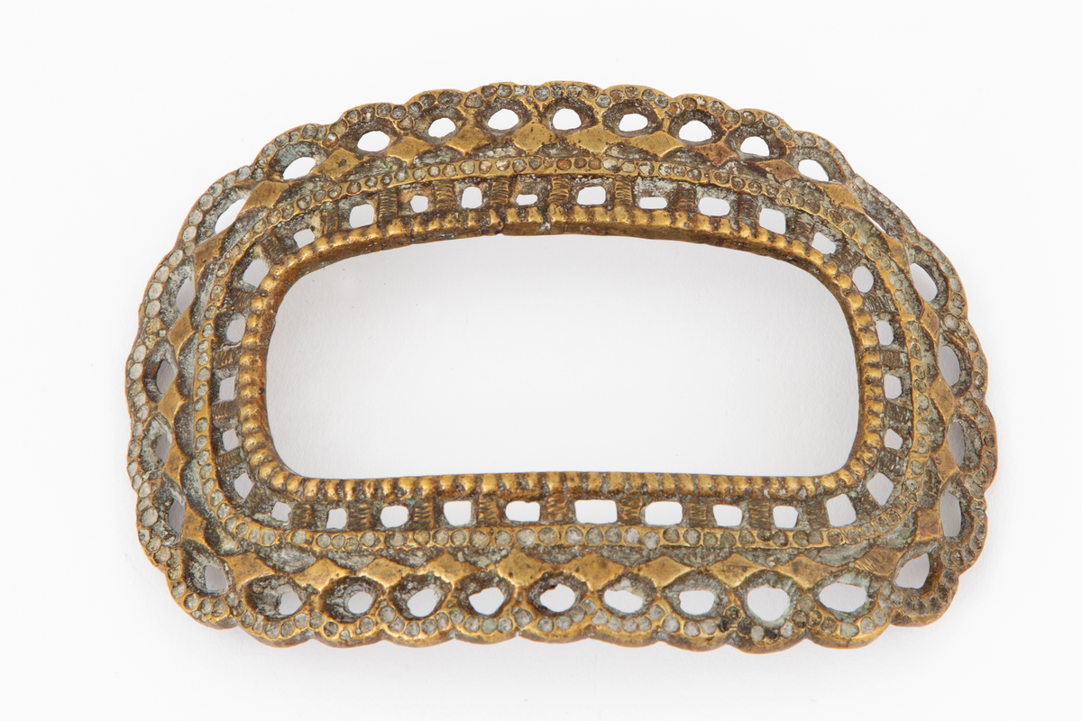 Skospenner støpt i krummet, oval form med tilsvarende innvendig åpning. Gjennombrutt med perlerader, groper, hull og ytterst tunget, gjennombrutt rand. Kun den ene spennen har stolpe med torn og feste med liten fast torn.