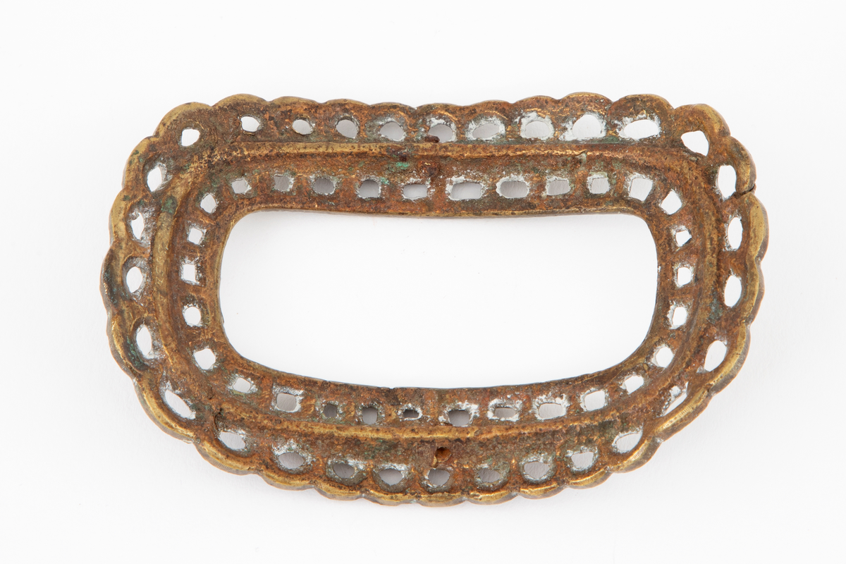 Skospenner støpt i krummet, oval form med tilsvarende innvendig åpning. Gjennombrutt med perlerader, groper, hull og ytterst tunget, gjennombrutt rand. Kun den ene spennen har stolpe med torn og feste med liten fast torn.