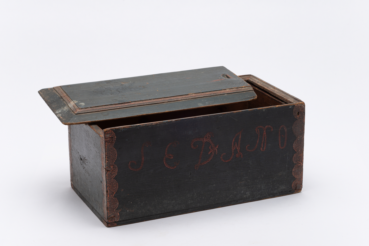 Rektangulær treeske (A) med tilhørende skyvelokk (B). Esken er malt sort med rød "rankedekor" i hjørnene (etterligning av metallbeslag). Rødmalt innskrift på langsidene (initialer og årstall). Sort lokk med rødt listverk. Lokket er velbrukt, og passer ikke lenger til esken (er for smalt). Esken ble brukt til oppbevaring av støpte lys.