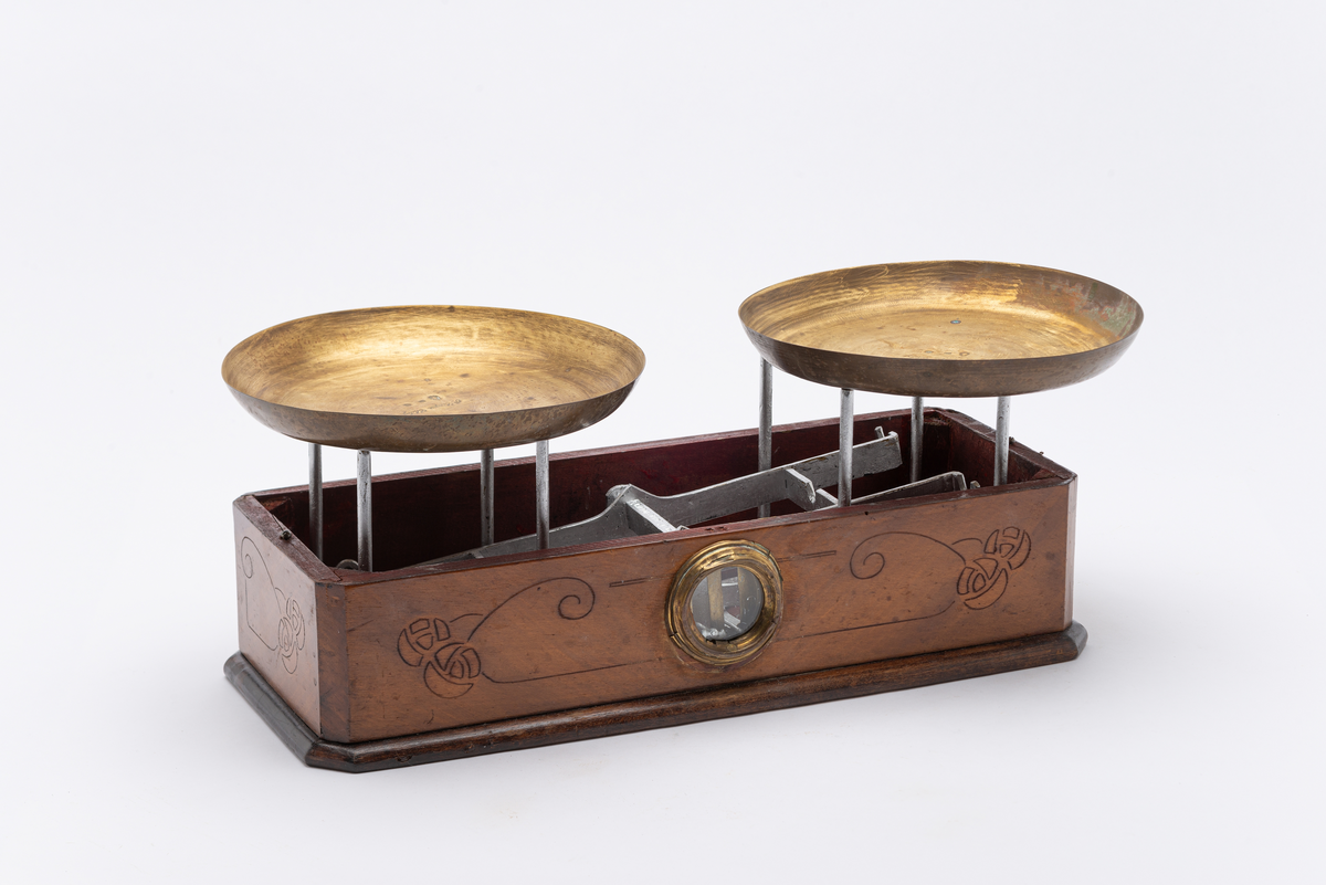 Kjøkkenvekt i åtte deler. Trekasse med vindu, glass med messingbeslag,  til balansestaver. Tekasse dekorert med blomstermotiver. Vippemekanisme, fem deler,  i metall inni trekassen. Åtte pigger stikkende opp av trekassen til å sette vektskålene på.